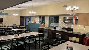 A restaurant with multiple tables and chairs, a counter with a display case, and a kitchen area. - Lively Inn & Suites (Sudbury)