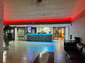 A hotel lobby with a reception desk, seating area, and a potted plant. - Lively Inn & Suites (Sudbury)