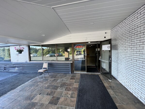 A building entrance with a glass door, a black mat, and a sign indicating 'OPEN'.