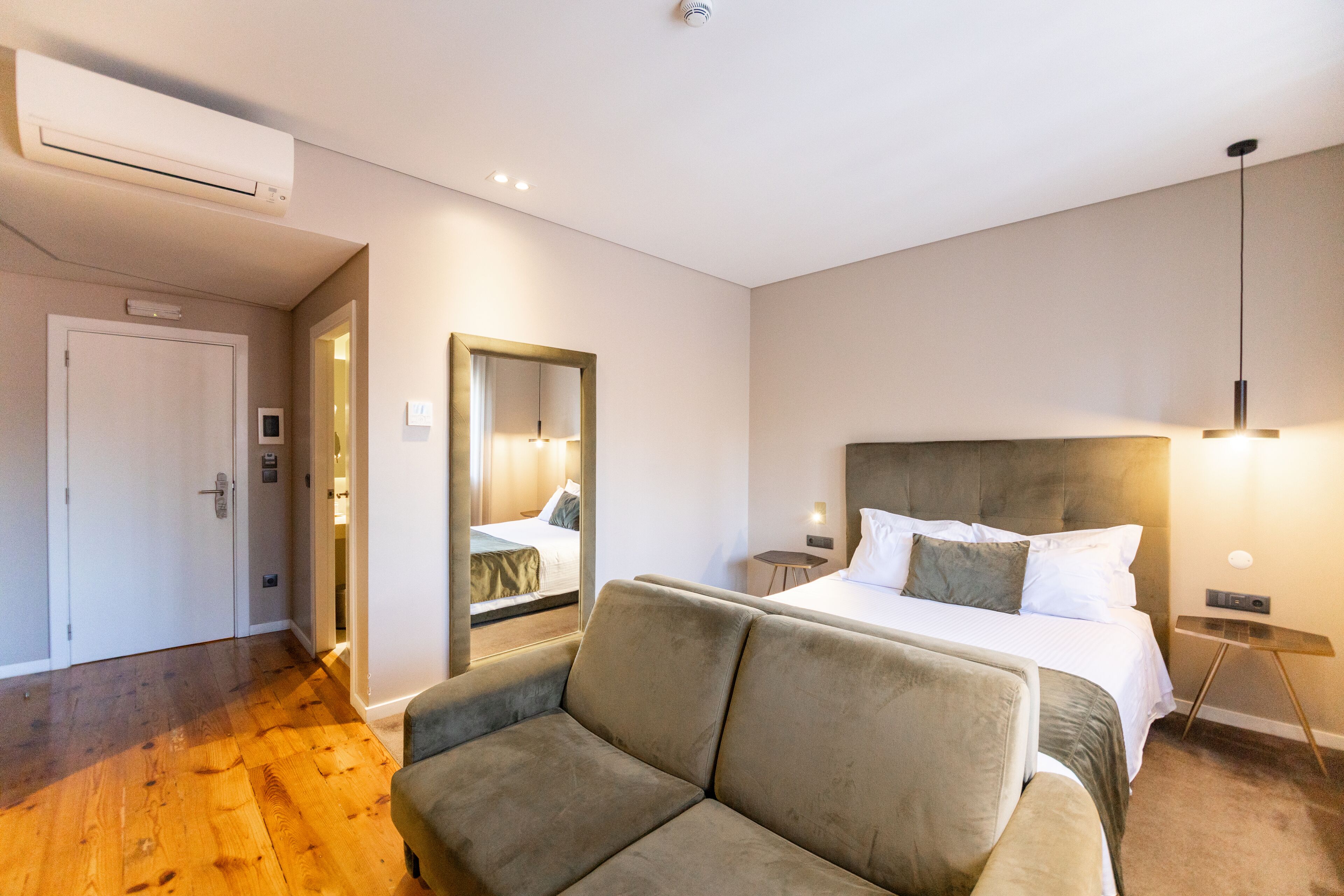 A hotel room with a bed, a sofa, a mirror, and a bedside table.