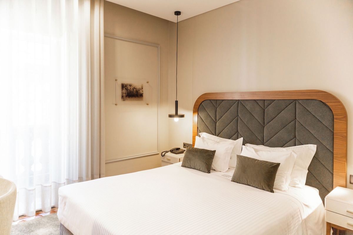 Une chambre d’hôtel avec un grand lit, une table de chevet, une commode, une lampe et une œuvre d’art accrochée au mur.