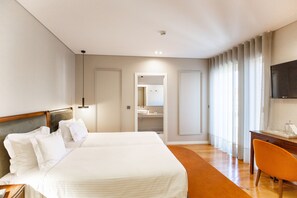 Habitación de hotel con una cama grande, un escritorio con silla, televisor y baño visible a través de una puerta abierta.
