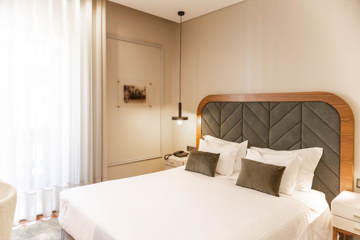 Una habitación de hotel con una cama grande, una mesita de noche, una lámpara y una obra de arte colgada en la pared.