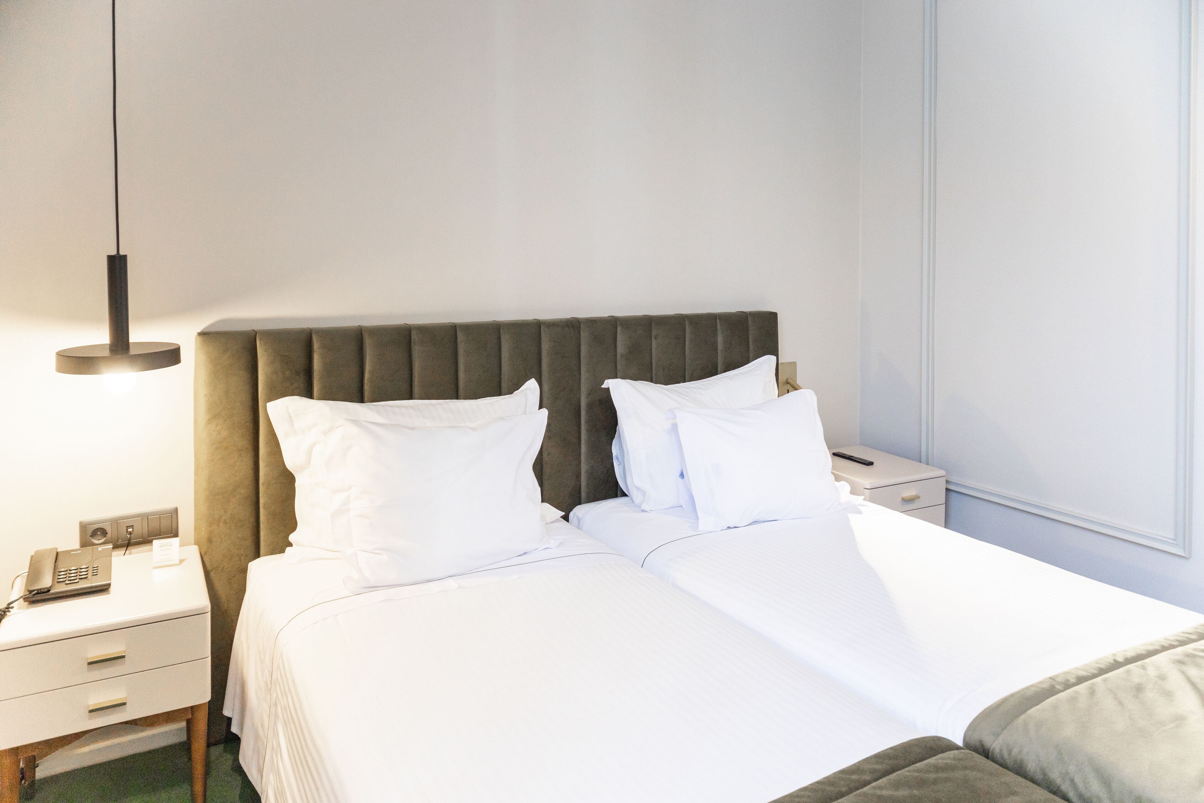 Una habitación de hotel con una cama, mesitas de noche, un teléfono y una ventana.