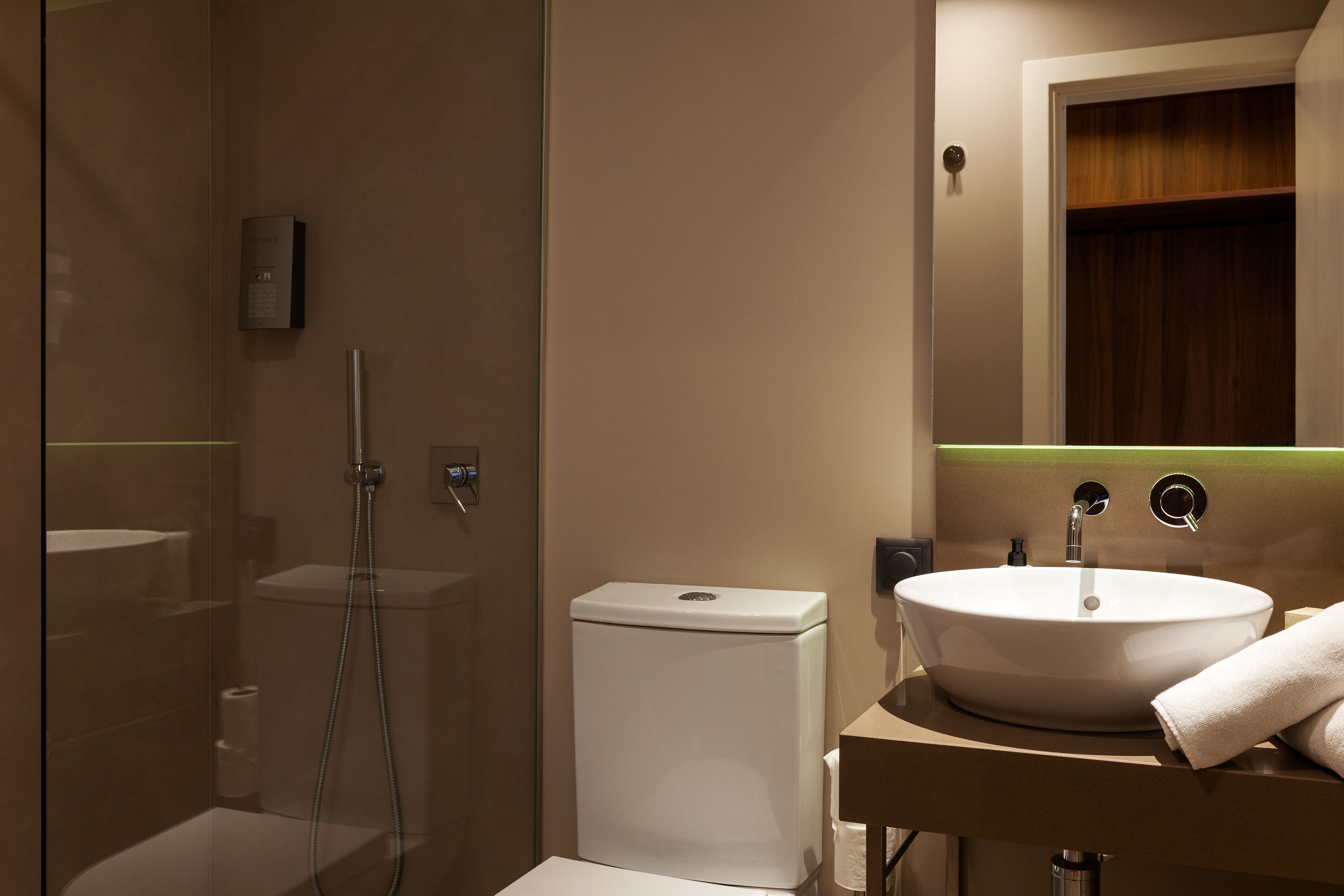 A modern bathroom with a glass-enclosed shower, a white toilet, and a sink with a mirror above.