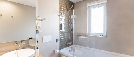 A modern bathroom with a large white sink, a toilet, a glass-enclosed shower, and a window.