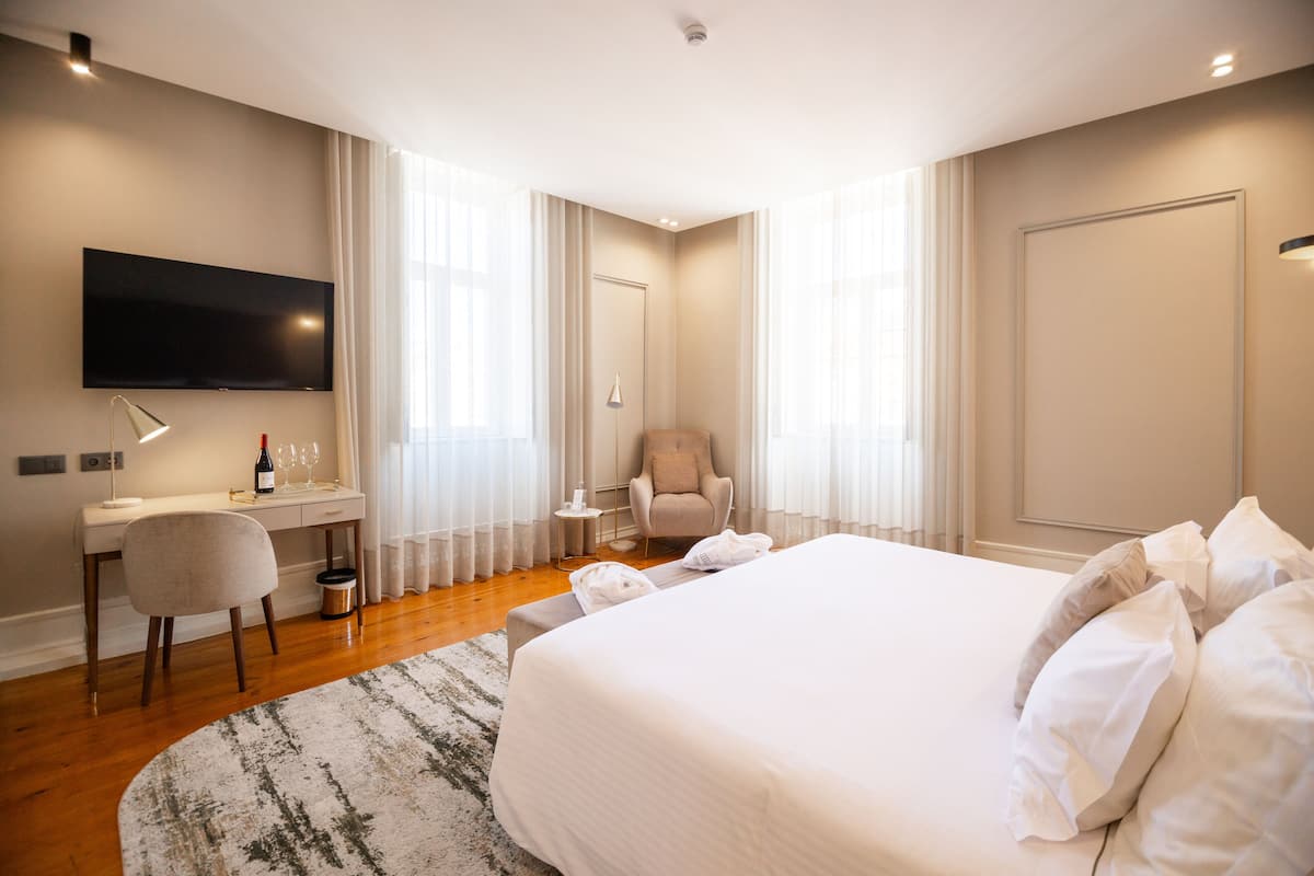 Una habitación de hotel con una cama grande, un escritorio con una silla, un televisor y un sillón con un cojín.