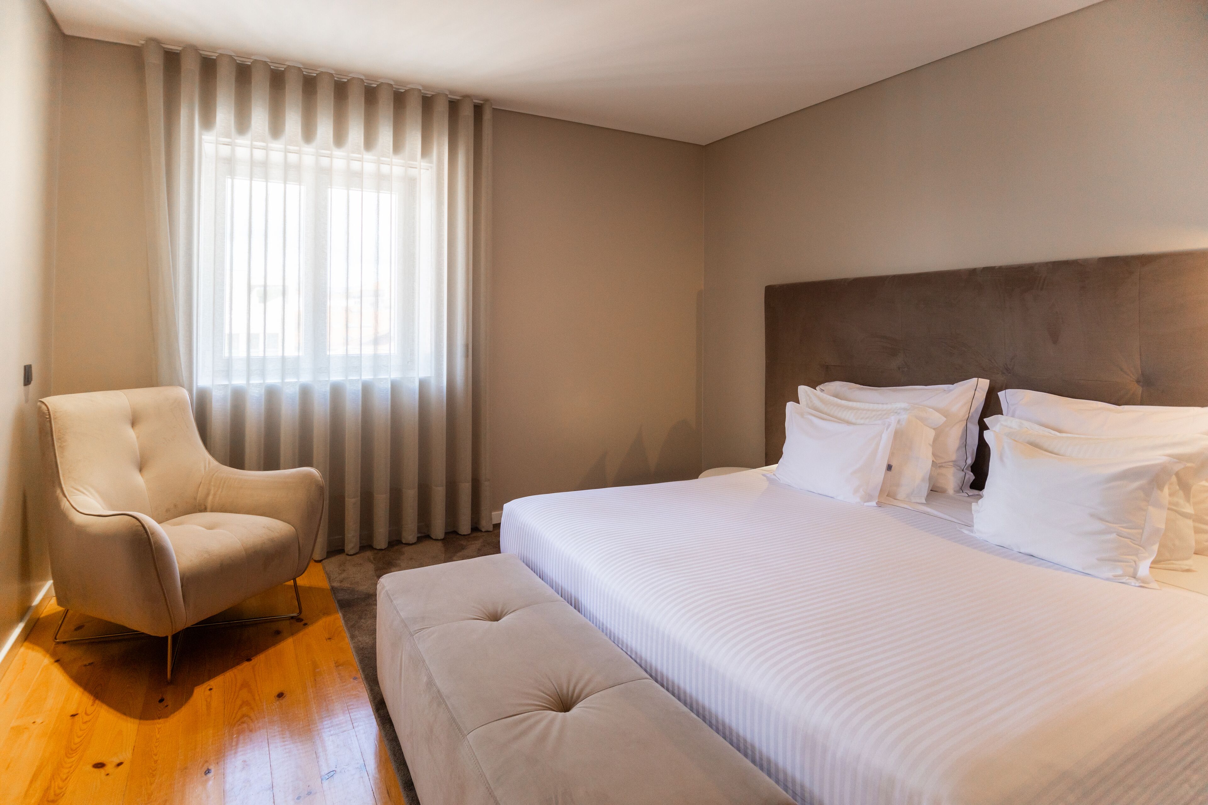 Un dormitorio con una cama grande, una silla y un ventanal con cortinas.