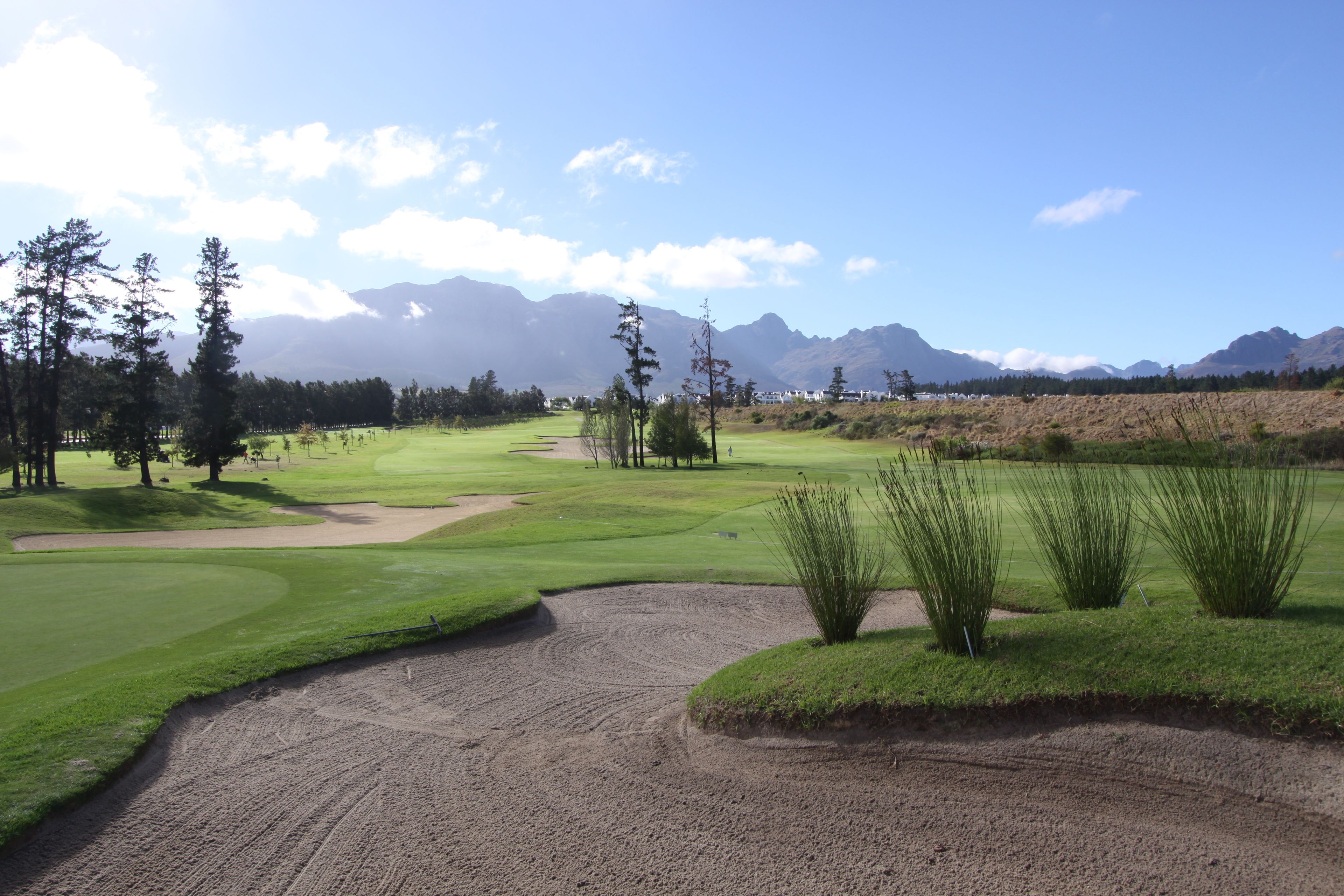 Un campo de golf con búnkeres de arena, árboles y montañas al fondo.