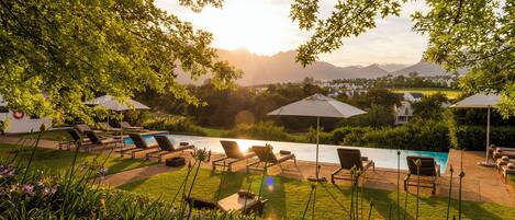 A pool area with lounge chairs and umbrellas, surrounded by greenery and a view of mountains.