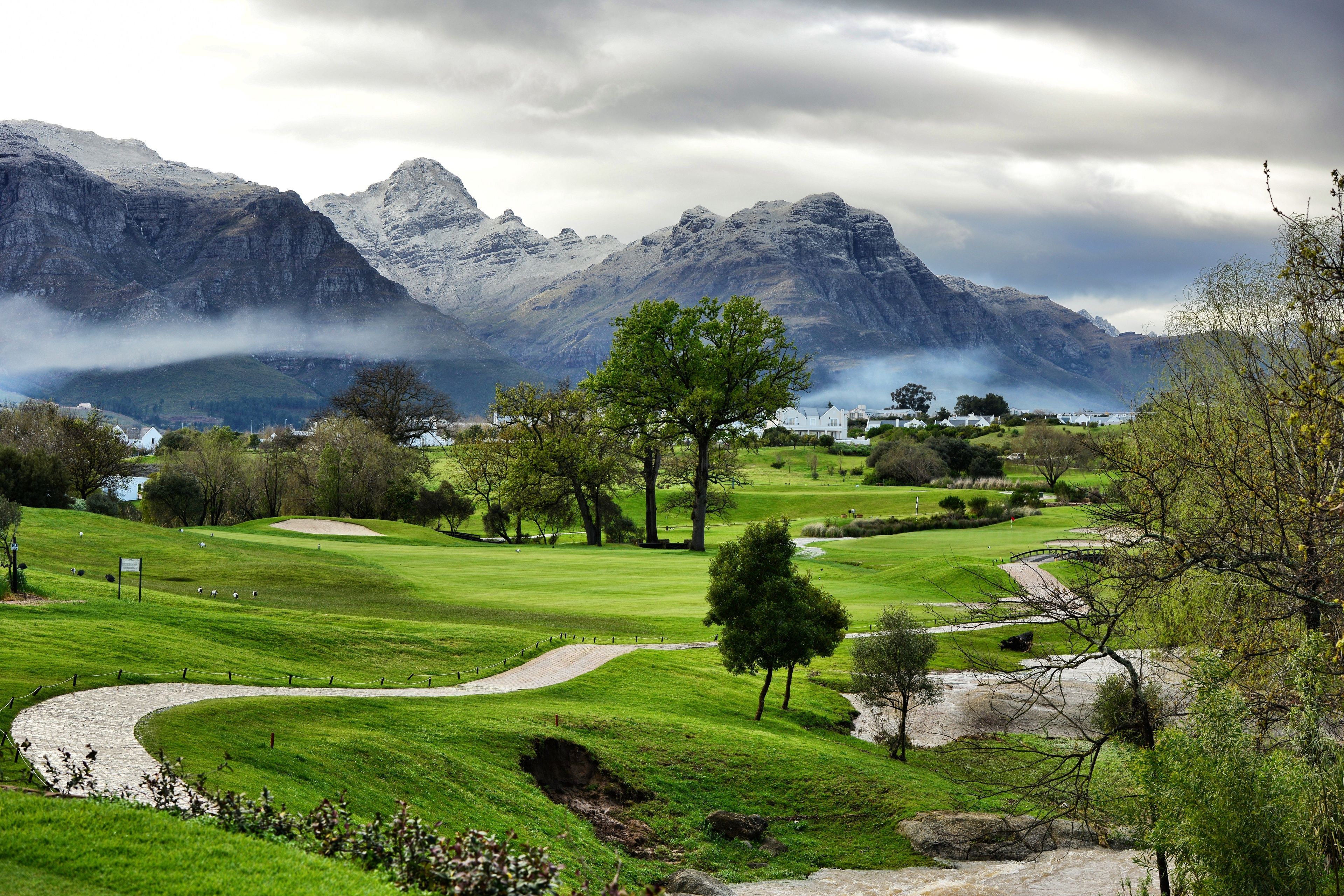 Ein Golfplatz mit einem gewundenen Weg, Bäumen und einem bergigen Hintergrund.
