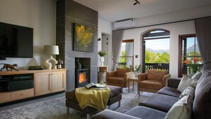 A modern living room with a fireplace, comfortable seating, a flat-screen TV, and a scenic view through large windows.