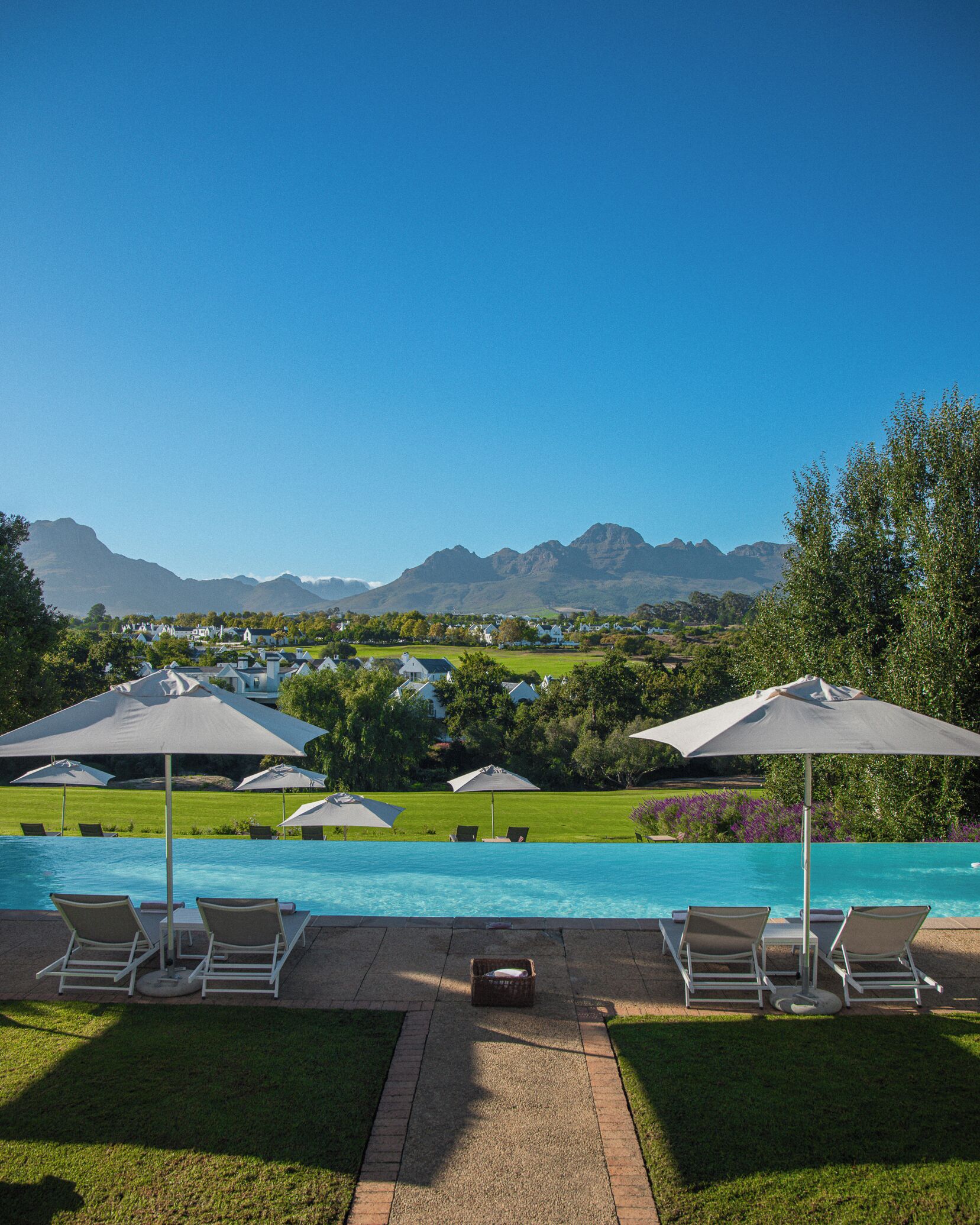 Un espace piscine doté de chaises longues et de parasols, une vue dégagée sur les montagnes et une pelouse bien entretenue.