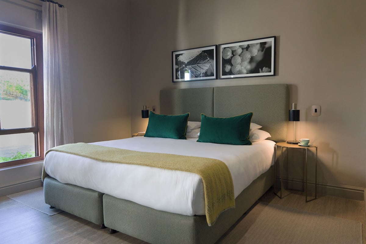 A neatly made bed with green and white bedding, a bedside table with a lamp, and two framed pictures on the wall.