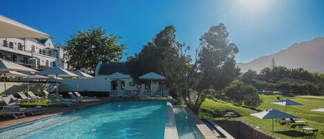 Piscina con sillas de descanso y sombrillas, rodeada de follaje y un paisaje montañoso.