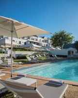 Una piscina con sillas de descanso y sombrillas, rodeada por un edificio con varios balcones.