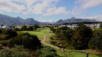 A golf course with a winding path, surrounded by greenery and mountains in the background.