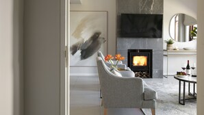 A modern living room with a fireplace, grey sofa, abstract painting, and a dining area with a table set for two.