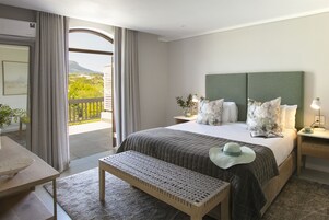 Ein Hotelzimmer mit einem großen Bett, einer Bank, einem Schreibtisch und einem Balkon mit Blick auf Grünflächen und ein Gebirge.