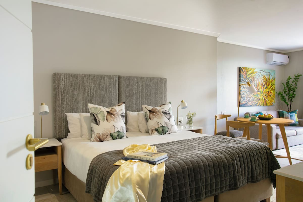 A neatly arranged bedroom with a bed, bedside tables, a small table with a bowl of fruit, and a painting on the wall.