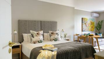 A neatly arranged bedroom with a bed, bedside tables, a small table with a bowl of fruit, and a painting on the wall.