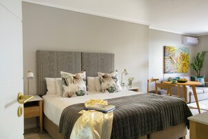 Un dormitorio ordenado con una cama, mesitas de noche, una pequeña mesa con un frutero y un cuadro en la pared.