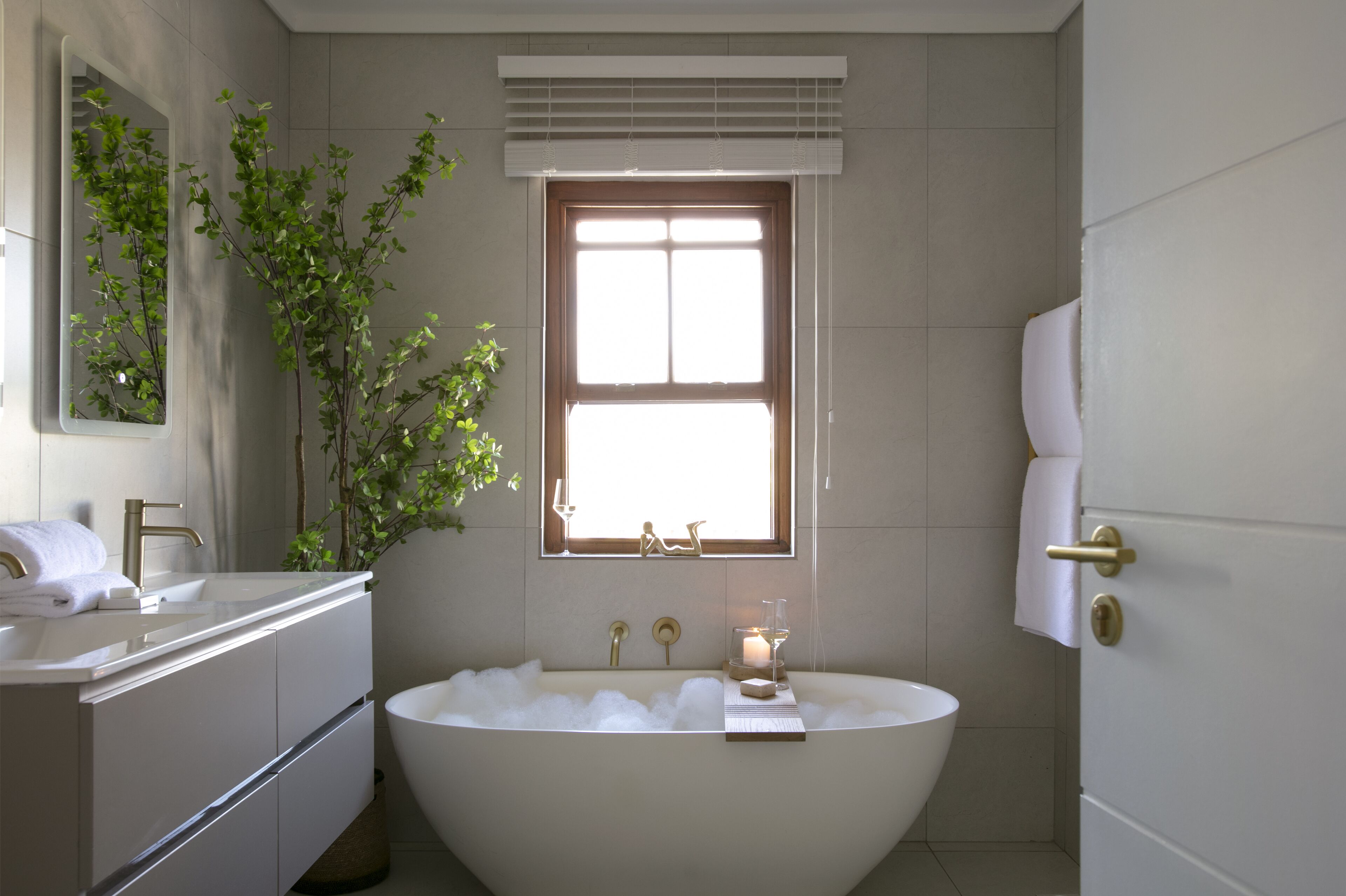 Un baño moderno con una bañera independiente, un tocador con espejo y una ventana con persianas.
