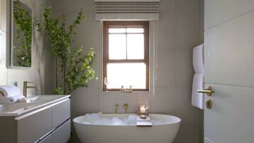 Un baño moderno con una bañera independiente, un tocador con espejo y una ventana con persianas.