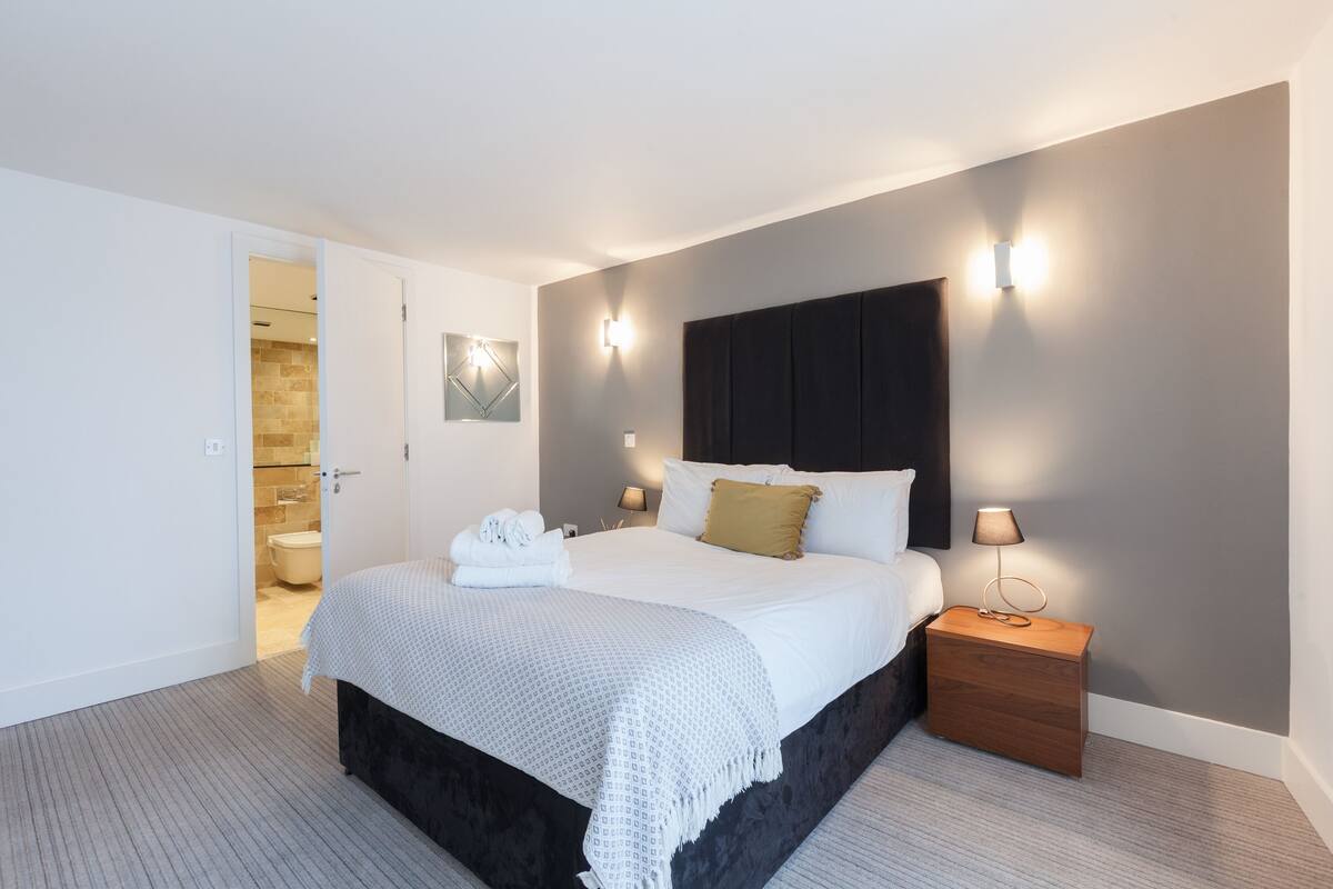 A modern hotel room with a large bed, bedside tables, and a bathroom visible through an open door.
