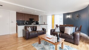 Un salon moderne avec deux canapés en cuir, une table basse en bois et une cuisine en arrière-plan.