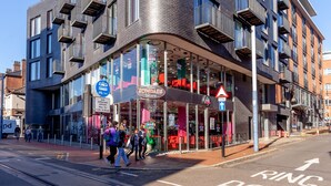 Un bâtiment moderne à la façade incurvée, doté de grandes fenêtres et d’une entrée au niveau du sol, avec une enseigne indiquant un magasin de glaces.