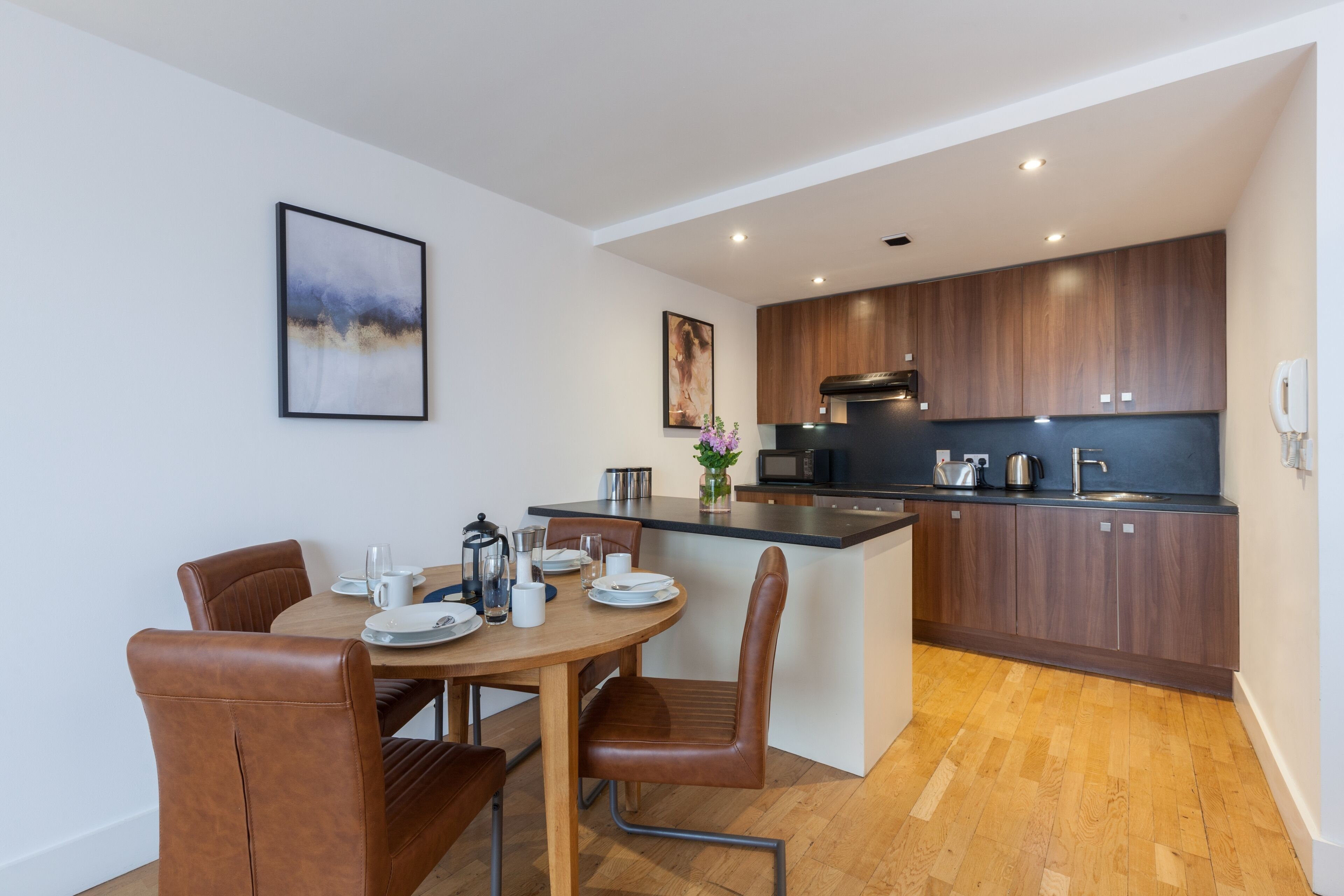 A modern kitchen with wooden cabinets, a central island, and a dining area with leather chairs.
