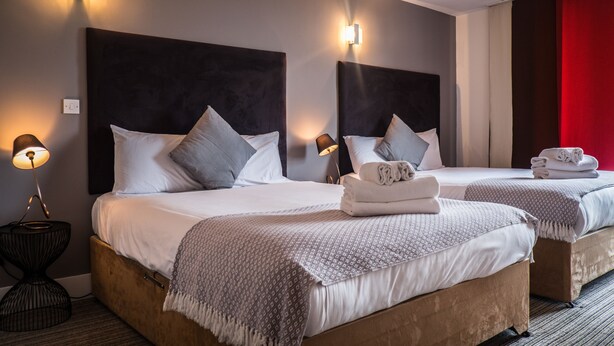 Une chambre d’hôtel avec deux lits, chacun doté d’une tête de lit, de lampes de chevet et d’un rideau rouge.