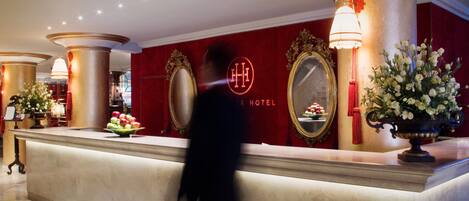 A hotel reception area with a marble counter, a large mirror, and a red wall with the hotel's name.