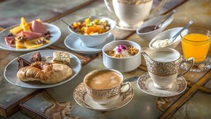 A breakfast table with a teapot, cups, plates of food, and a glass of orange juice.
