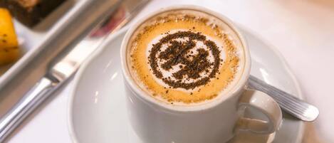 Una taza de café con arte de latte sobre un plato, una cuchara y un vaso de zumo de naranja en una bandeja.