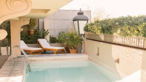 A swimming pool with two sun loungers, a potted plant, and a lamp post.