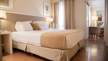 A hotel room with a large bed, bedside tables, a chair, and a door leading to another room.
