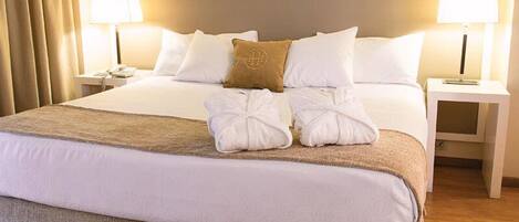 A hotel room with a large bed, two bedside lamps, a headboard, and a framed picture on the wall.