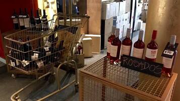 A wine shop interior with carts filled with wine bottles, a sign reading "ROGADOS", and a chalkboard with handwritten text.