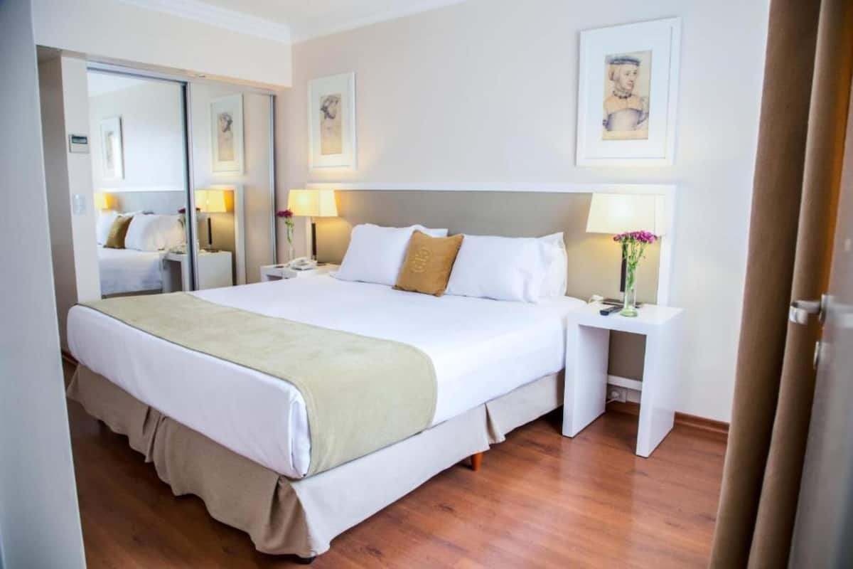 A hotel room with a large bed, bedside tables with lamps, a mirror, and framed artwork on the walls.