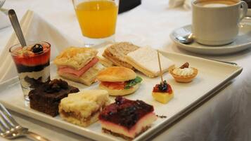 A variety of desserts and sandwiches on a white rectangular plate, accompanied by a glass of orange juice and a cup of coffee on a table.