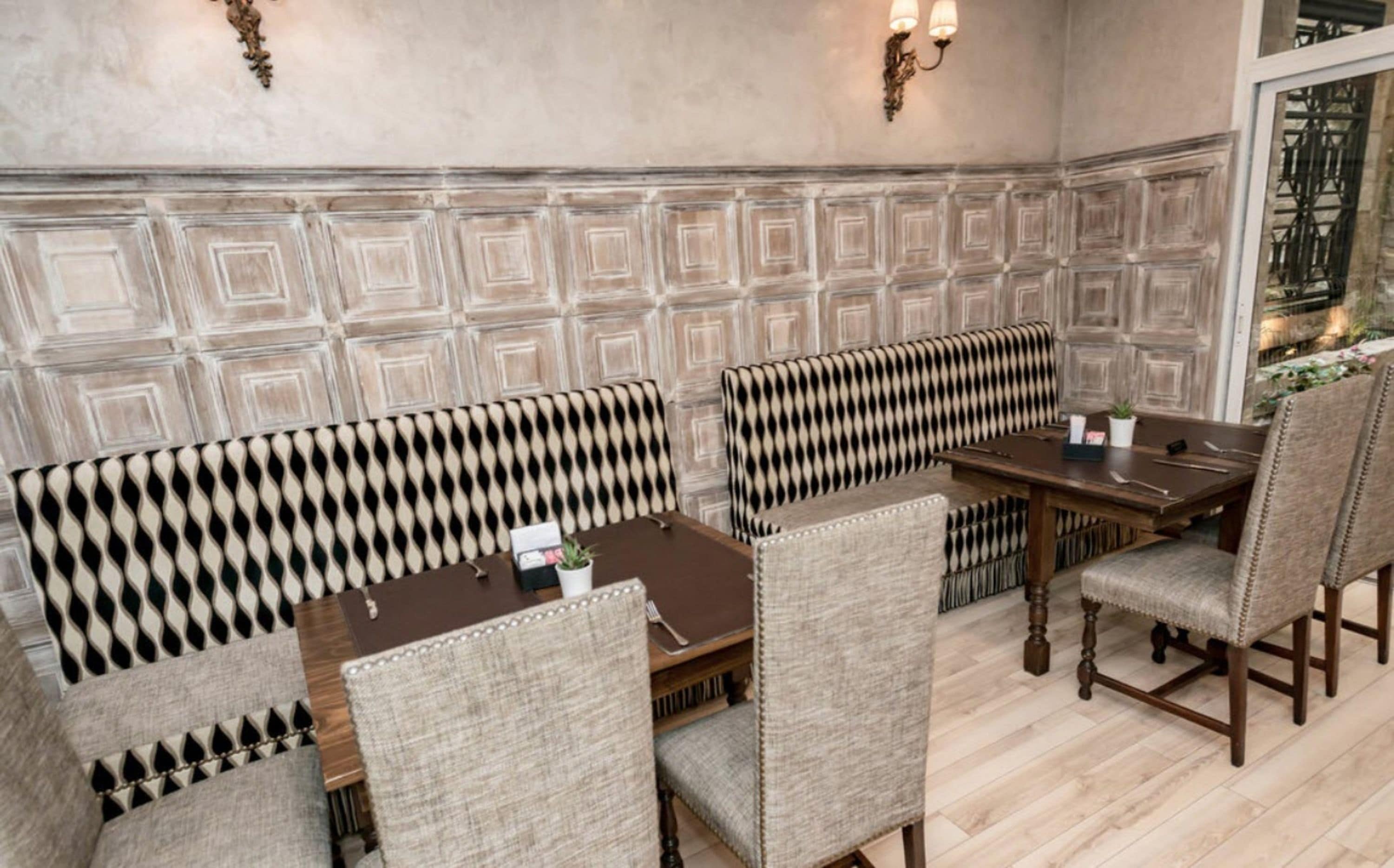 A dining area with a patterned bench seating, a wooden table, and a wall with a geometric design.