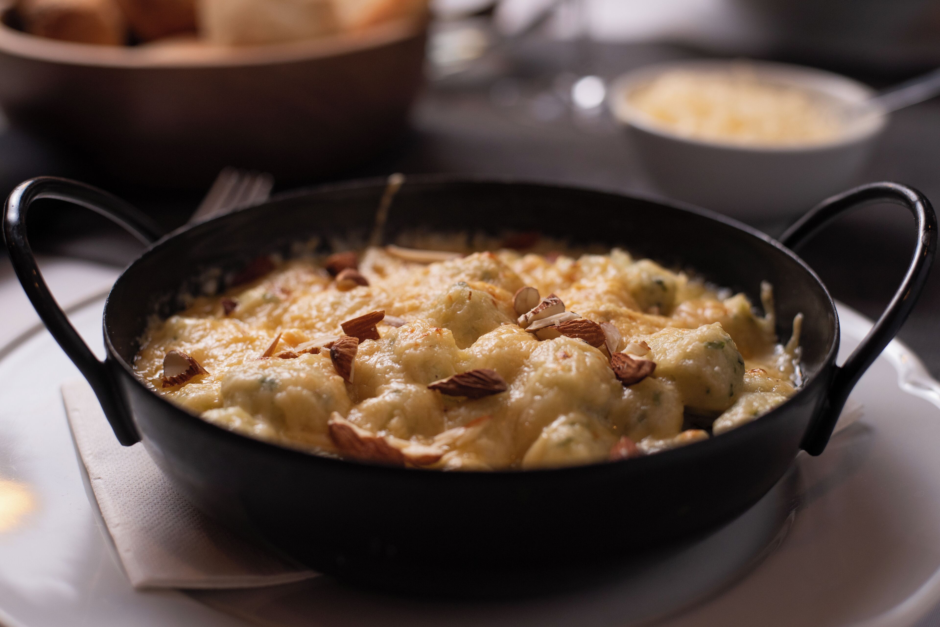 A black skillet with a creamy dish garnished with nuts, placed on a white napkin.