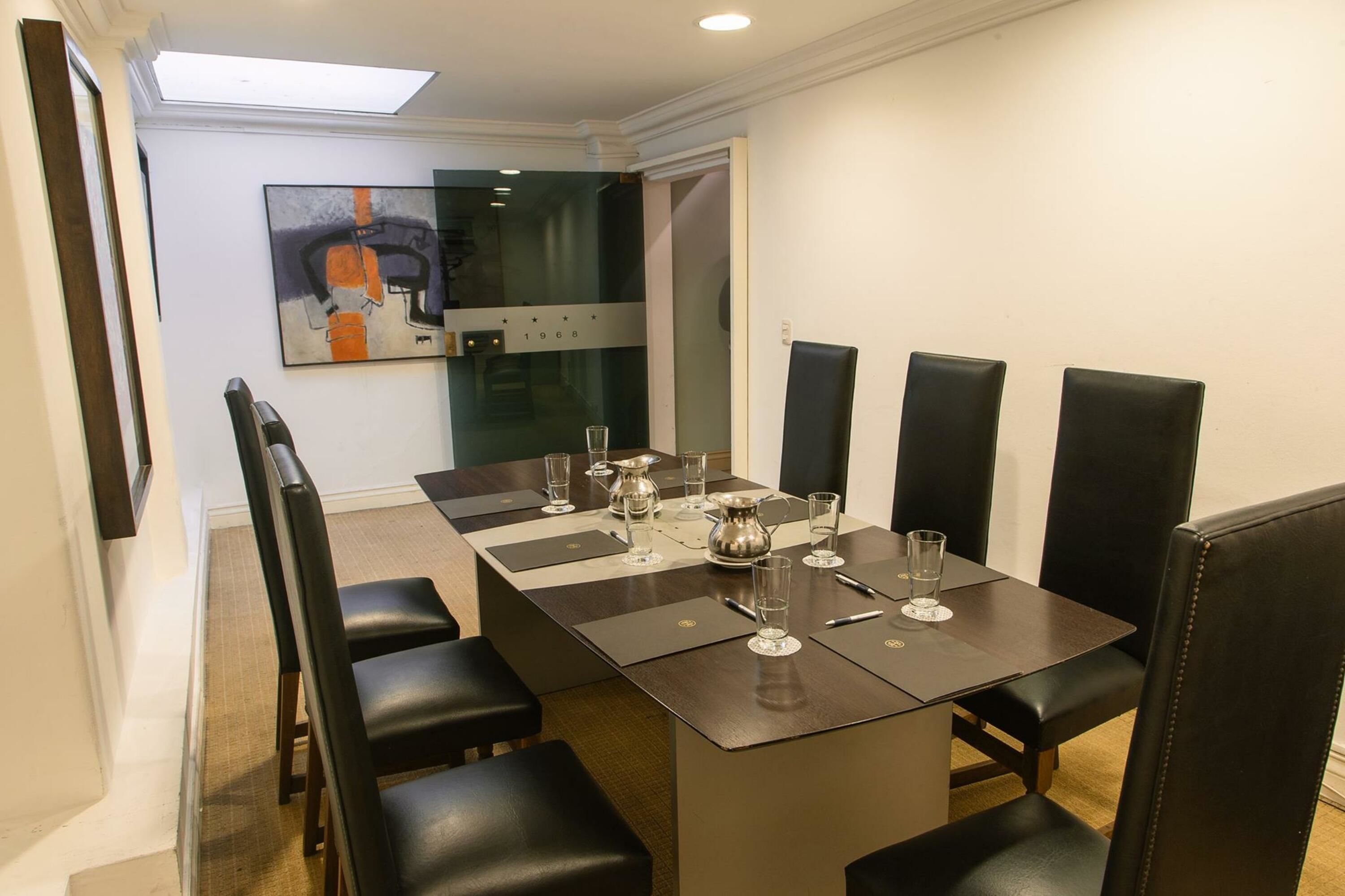 Een vergaderzaal met een lange tafel, zwarte stoelen en een schilderij aan de muur.