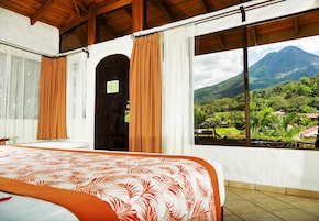 A bedroom with a bed, a door, and a window with a view of a mountain and greenery.
