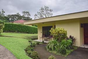 Edificio de una sola planta con un porche cubierto, un pequeño jardín con diversas plantas y un sendero pavimentado que conduce a la entrada.