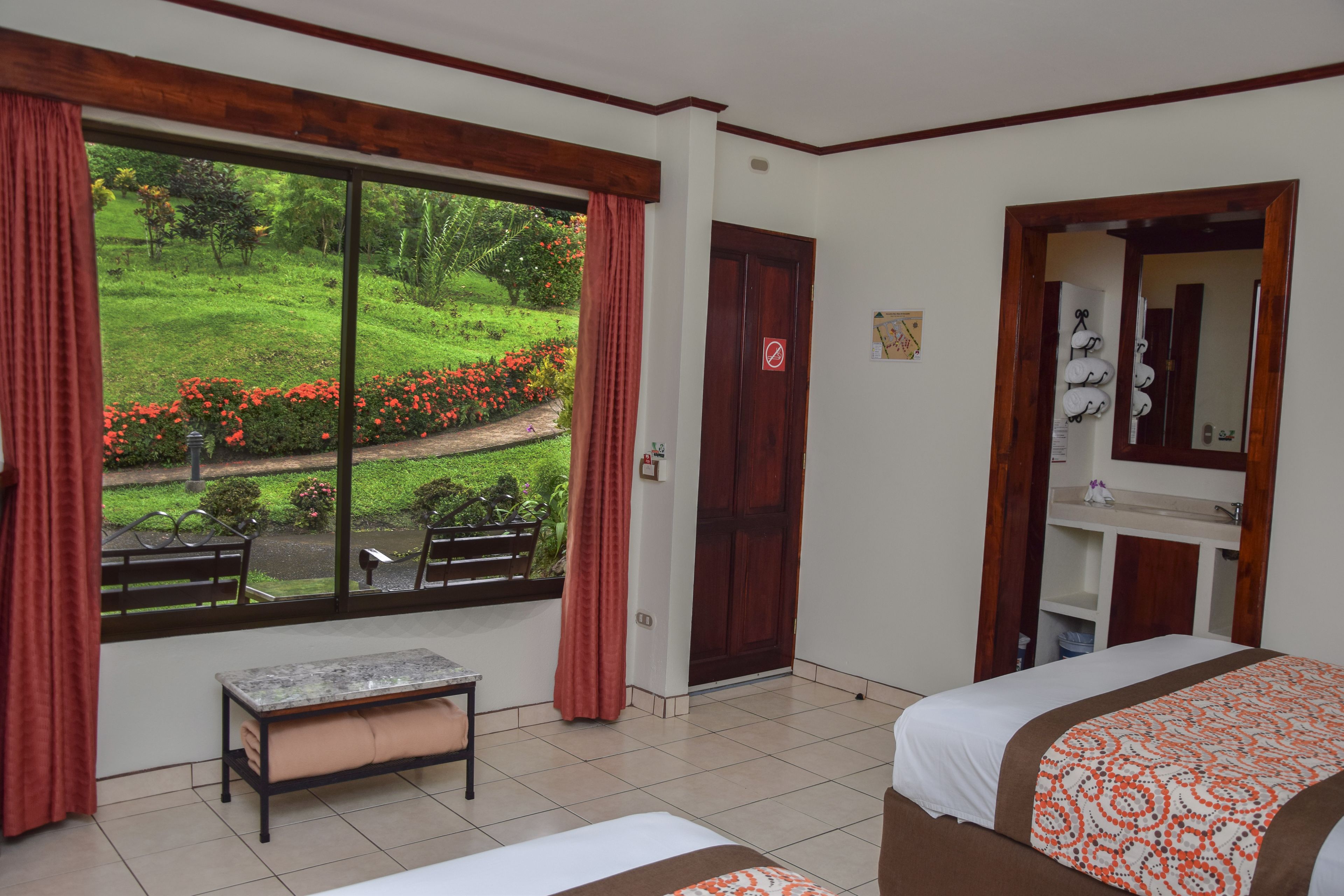 A hotel room with a large window, a bed, a bench, and a small table.
