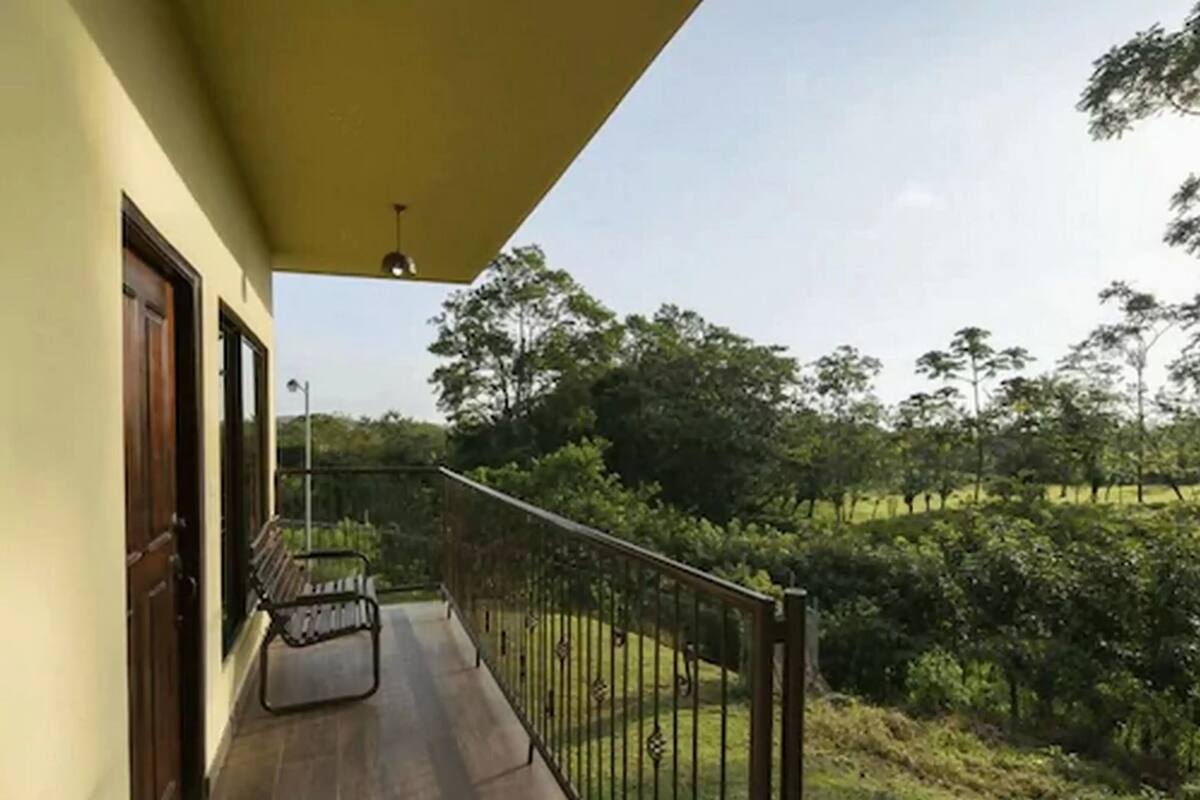 A balcony with a bench, a railing, and a view of a green landscape.