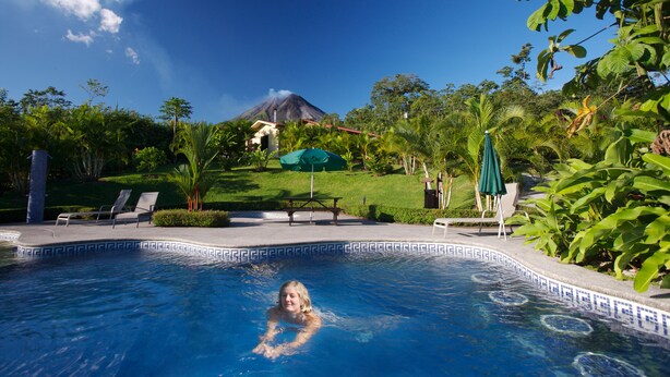 A swimming pool with lounge chairs and a view of a volcano in the background.